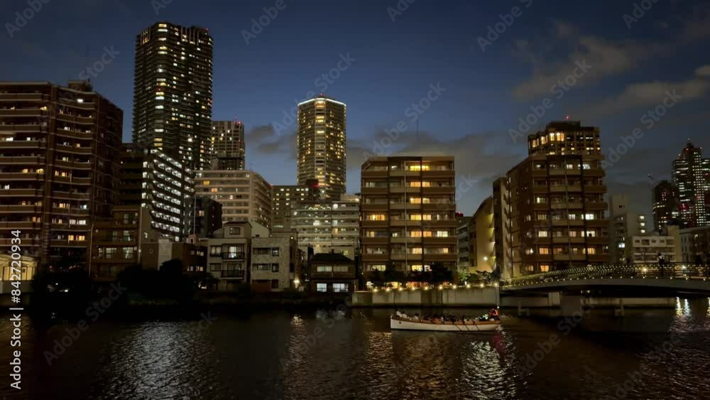 City skyline and river at dusk with a boat passing by illuminated buildings City skyline and river at dusk with a boat passing by illuminated buildings