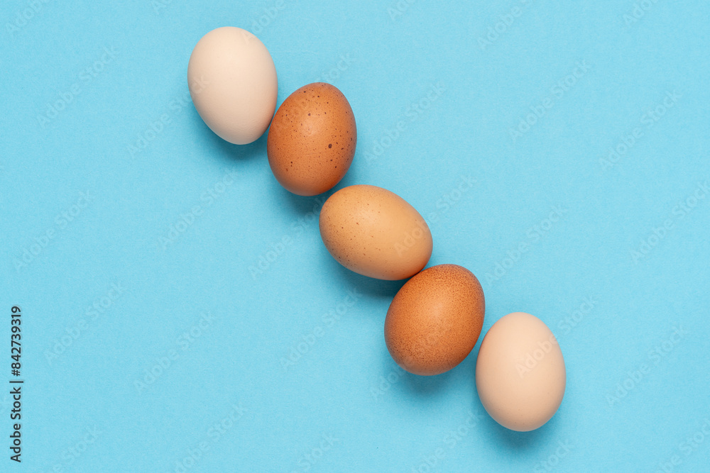 Multi-colored farm eggs neatly stacked on blue background Multi-colored farm eggs neatly stacked on blue background