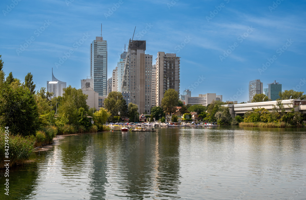 Vienna, Austria, August 17, 2022. View of the Alte Donau nature park. The modern skyscrapers stand out behind a small harbor with boats for rent. People relax here. Vienna, Austria, August 17, 2022. View of the Alte Donau nature park. The modern skyscrapers stand out behind a small harbor with boats for rent. People relax here.