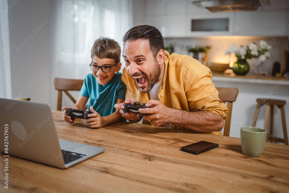 Father and son play video games on laptop with joystick at home Father and son play video games on laptop with joystick at home