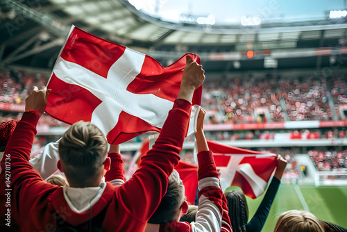 Fans waving the flag of Denmark at a football match, with the stadium crowd in the background
