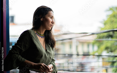 Retrato de una joven latina de pelo largo vestida con ropa cómoda mientras observa su entorno desde un balcón. photo