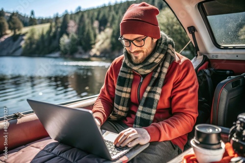 A man wearing a red hat and scarf is sitting in a car and using a laptop photo
