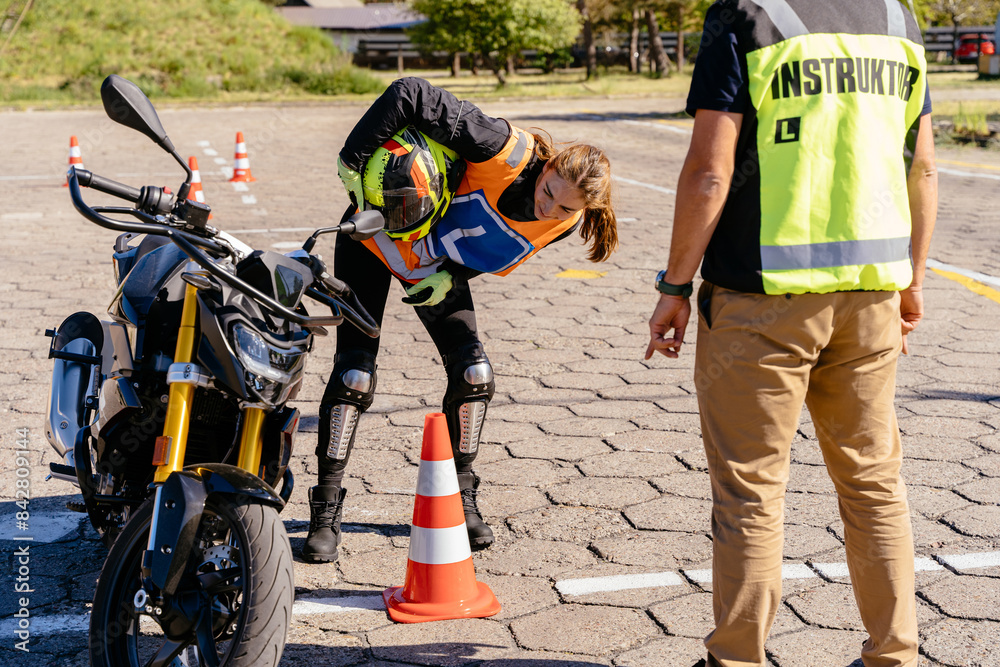Fototapeta premium Learner biker on test road with red cones. Instructor writing on clipboard his points.