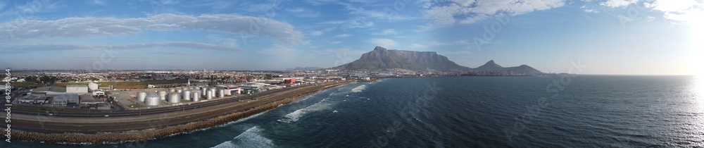 Obraz premium Panoramic photo of coastline close to Cape Town showing Table Mountain and industrial area with railway track.
