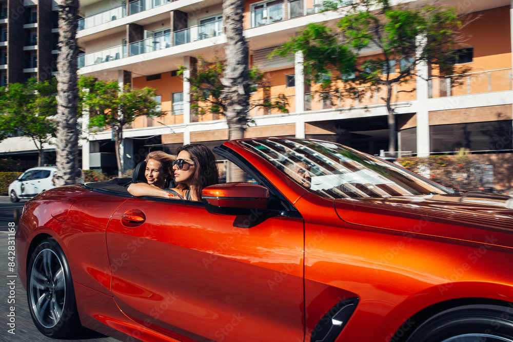 Fototapeta premium Two girls are driving in a convertible around the city