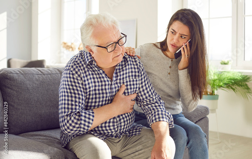 Vászonkép Portrait of worried young woman daughter holding mobile phone and calling emergency ambulance to her senior old father parent with heart attack at home