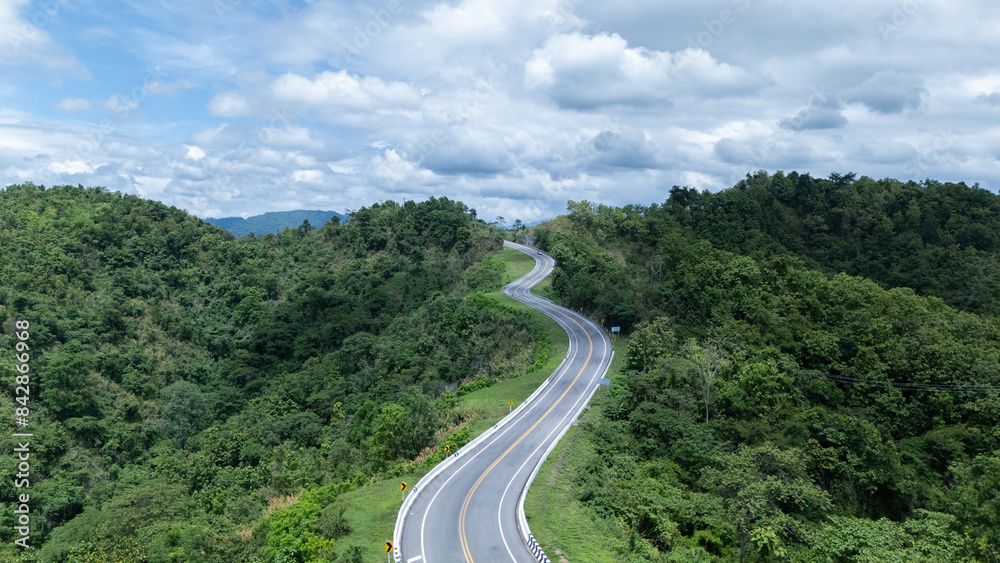 Aerial view from above of country road through the green summer forest in summer Thailand. Top view of the asphalt road and dense green forests. Aerial view from above of country road through the green summer forest in summer Thailand. Top view of the asphalt road and dense green forests.