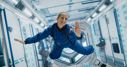 Fotografie Portrait of a Courageous Caucasian Female Astronaut on Board a Spacecraft, Floating in Zero Gravity and Smiling At The Camera, Waving