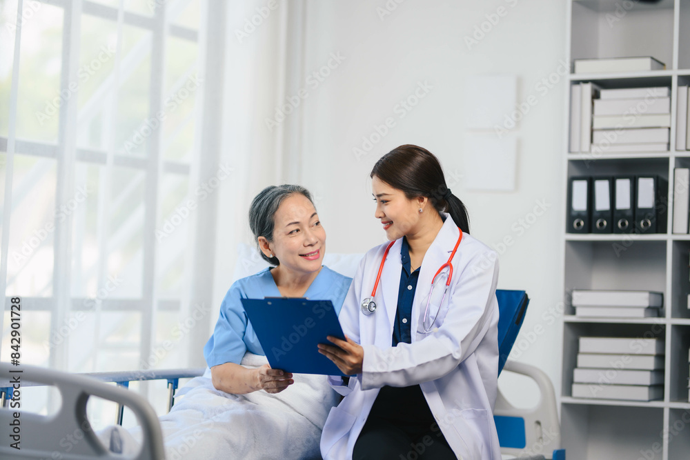 Fototapeta premium A woman in a white coat is sitting next to an older woman in a hospital bed