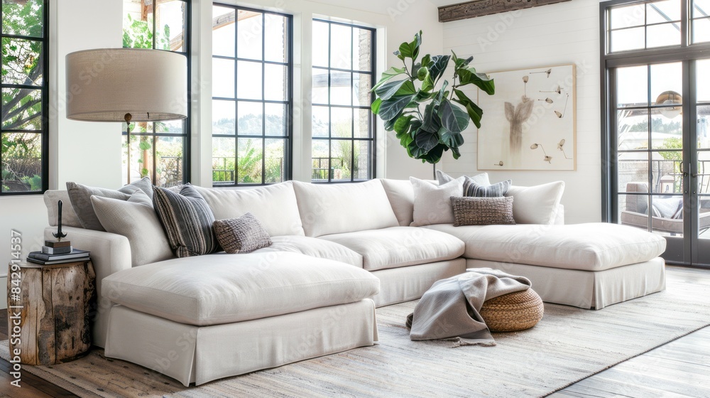 Fototapeta premium A white sectional sofa in a modern living room with large windows and natural light