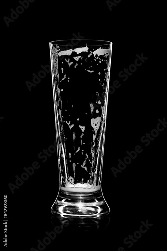 Photos Empty beer glass with residue foam and bubbles, set against a black background