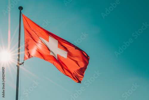 Close-up of a Swiss flag waving in the wind against a clear blue sky, with the red fabric and white cross clearly visible and vibrant in the sunlight