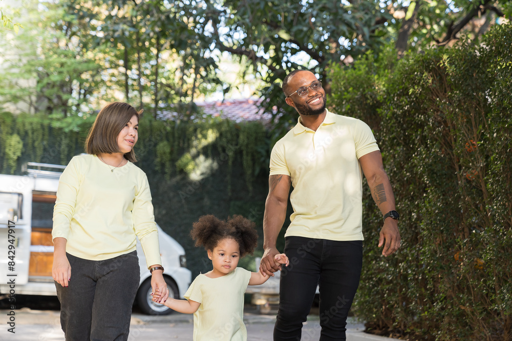 African American father and Asian mother holding hands little daughter during playing and walking together in garden African American father and Asian mother holding hands little daughter during playing and walking together in garden