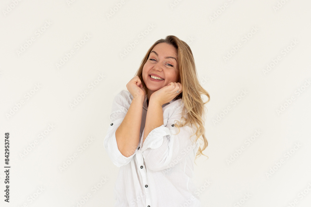 Headshot of pleased high spirit pretty female model, has warm pleasant smile, keeps hands under chin, wears white shirt, isolated over white background. Happiness concept Headshot of pleased high spirit pretty female model, has warm pleasant smile, keeps hands under chin, wears white shirt, isolated over white background. Happiness concept