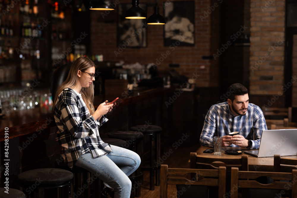 Two young people, husband and wife, Pub owners, working in their cafeteria, cleaning and calculating before opening time. Man and woman work in coffee shop, ordering drinks from delivery company Two young people, husband and wife, Pub owners, working in their cafeteria, cleaning and calculating before opening time. Man and woman work in coffee shop, ordering drinks from delivery company