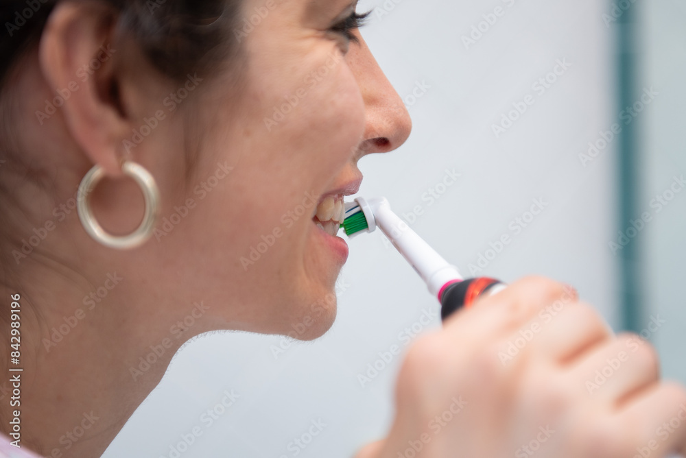 Beautiful woman is brushing her teeth with electric toothbrush in bathroom in the morning Beautiful woman is brushing her teeth with electric toothbrush in bathroom in the morning