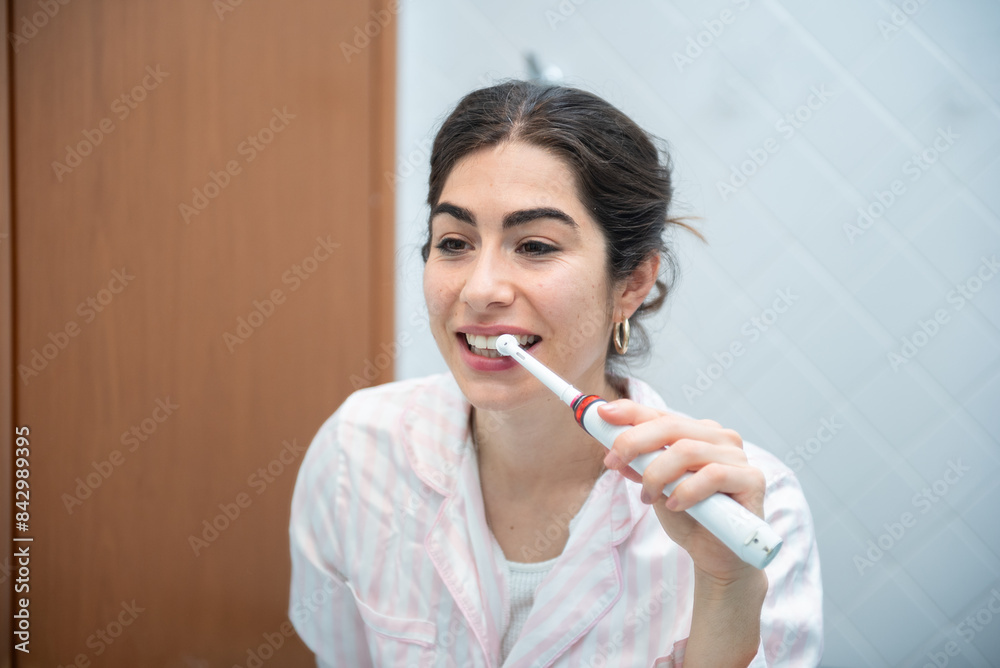 Beautiful woman is brushing her teeth with electric toothbrush in bathroom in the morning Beautiful woman is brushing her teeth with electric toothbrush in bathroom in the morning