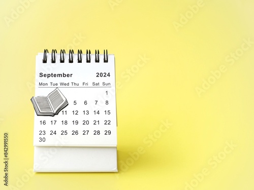 Desk calendar for September 2024 with a drawing of a book on a yellow background with copy space. Back-to-school concept