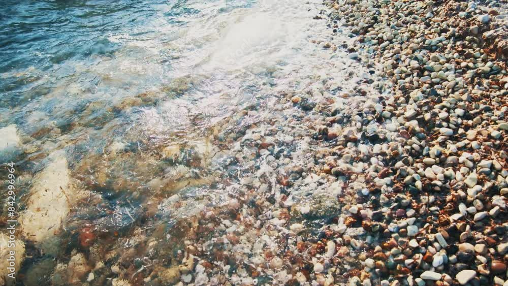 Vibrant waves gently washing over a pebbled beach, creating contrast between smooth, multicolored stones and sparkling water.