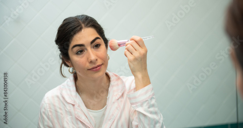 Young woman applying fard while looking in the mirror in bathroom