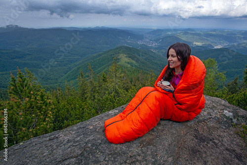 Woman tourist  with coffee cup in orange sleeping bag on the rock in Carpathian mountains photo