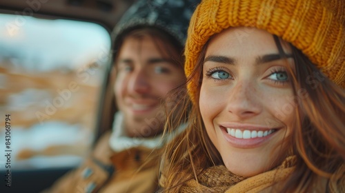 A smiling woman with striking blue eyes and a yellow beanie exudes warmth in a wintery setting, sitting beside a male companion © svastix