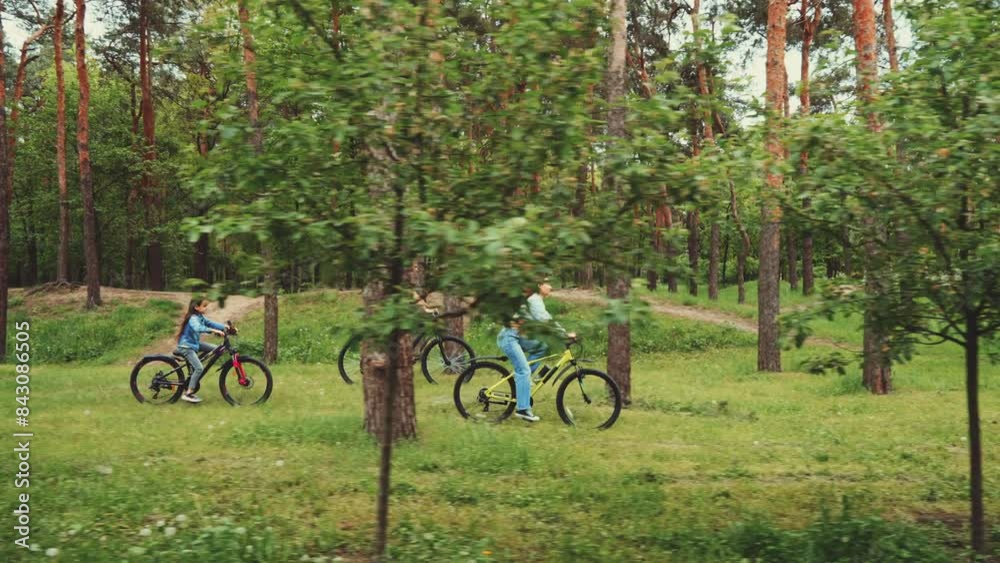 Father, daughter, and mother riding bikes together on forest trail. Green trees and grass surround them. Concept of family bonding and healthy lifestyle Father, daughter, and mother riding bikes together on forest trail. Green trees and grass surround them. Concept of family bonding and healthy lifestyle
