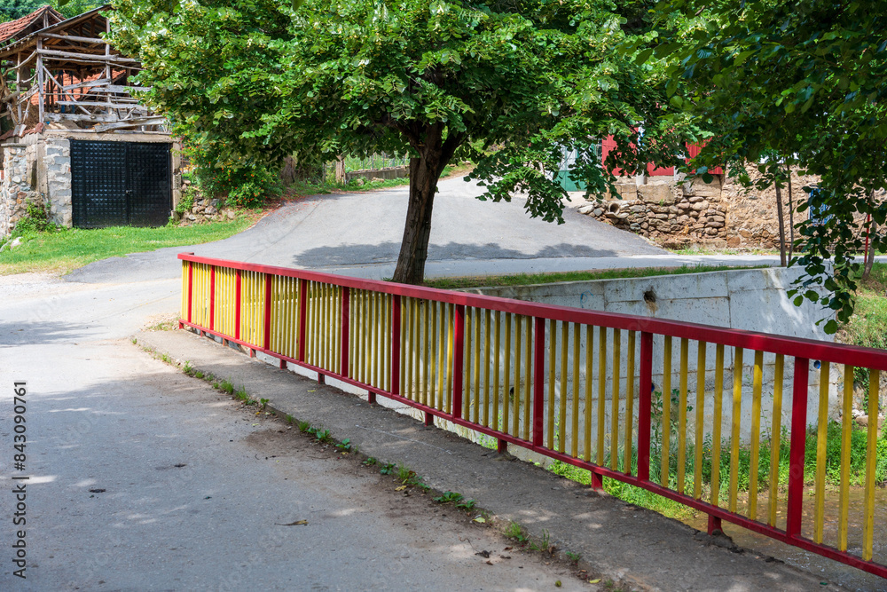 Rural Charm. Colorful Bridge Fence with Yellow and Red Paint, Black Garage Door Framed by Trees Rural Charm. Colorful Bridge Fence with Yellow and Red Paint, Black Garage Door Framed by Trees