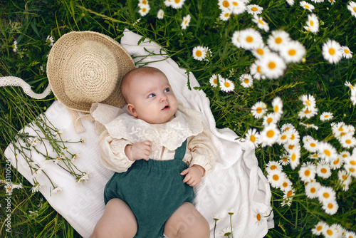 Obraz na płótnie beautiful chubby little girl infant baby lying in a field with daisies in a hat on a summer afternoon in nature w salonie