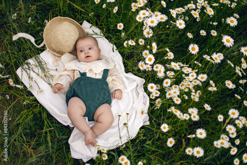 beautiful chubby little girl infant baby lying in a field with daisies in a hat on a summer afternoon in nature
