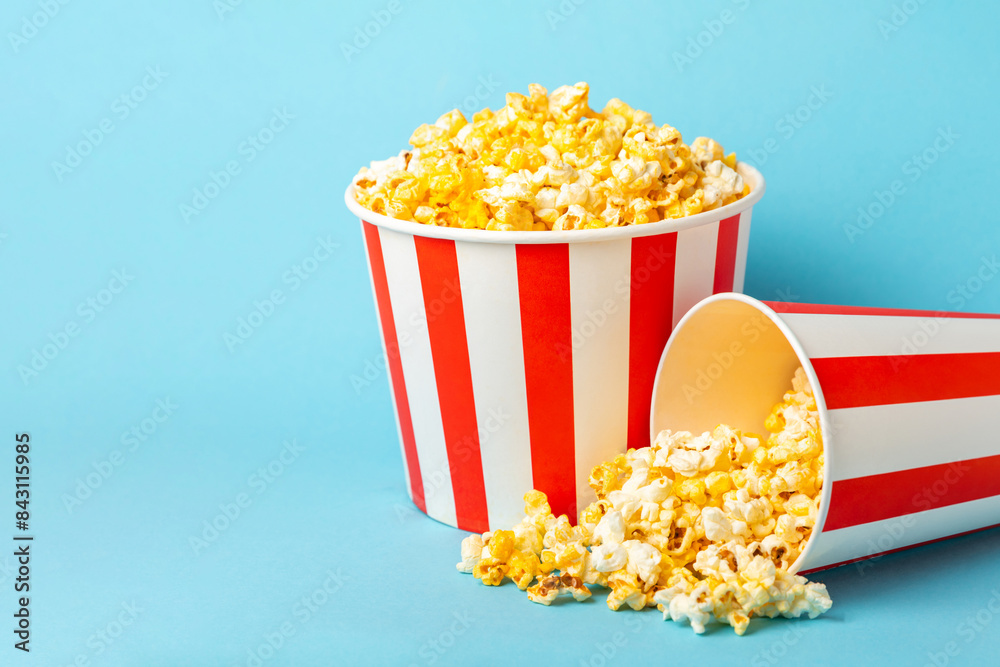 Popcorn box. Red and white striped buckets of popcorn on a blue background. Cinema and entertainment concept. Movie night with popcorn. Cheesy popcorn. Delicious appetizer, snack. Place for text. Popcorn box. Red and white striped buckets of popcorn on a blue background. Cinema and entertainment concept. Movie night with popcorn. Cheesy popcorn. Delicious appetizer, snack. Place for text.