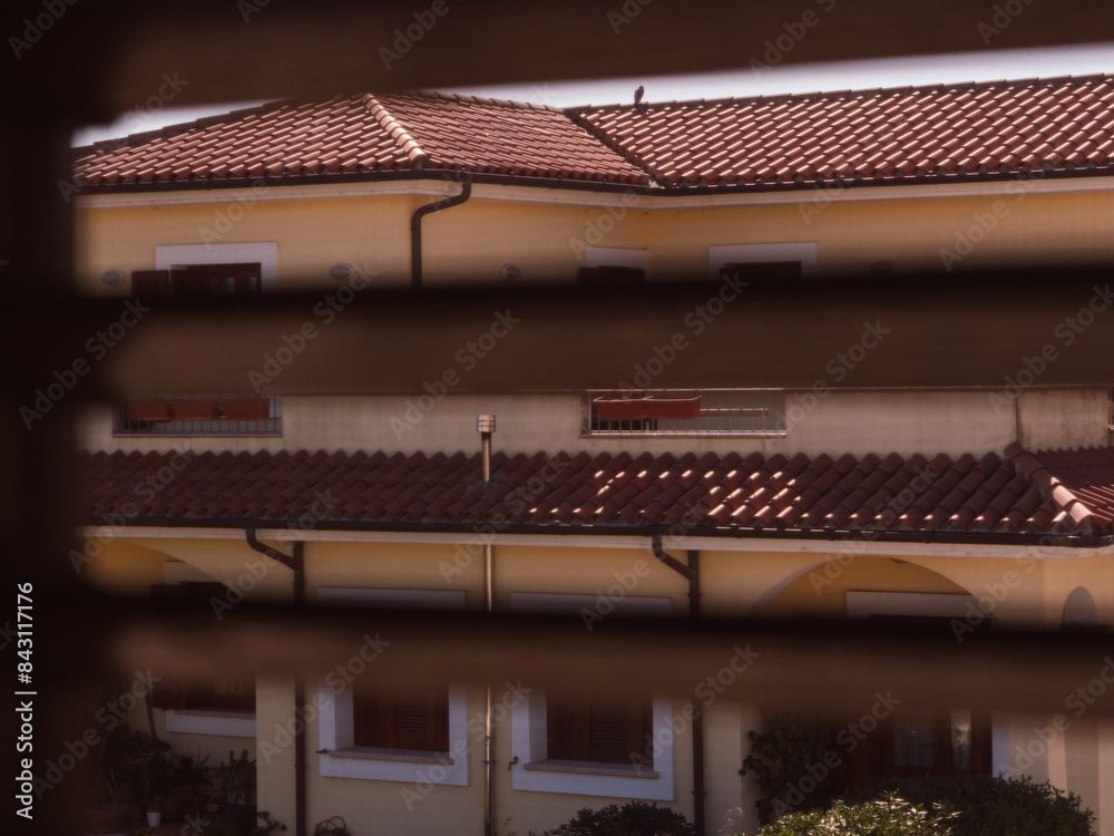 Window Blinds View: A horizontal shot of a two-story Italian house in Sardinia, framed through the window blinds from a window across the street. Window Blinds View: A horizontal shot of a two-story Italian house in Sardinia, framed through the window blinds from a window across the street.