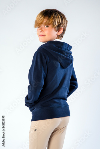 Portrait of a young boy in a hoodie, wearing riding pants, standing with his hands in his pockets looking over his soulder photo