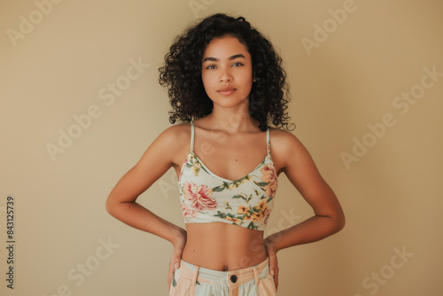 20 years old  latina woman in floral crop top posing confidently with hands on hips against a neutral background photo