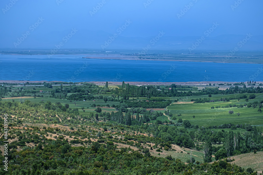 Wide field landscape photo. Looking down from the hill. Sparse trees, grass and lakeunder the clear sky. Konya, Turkey.