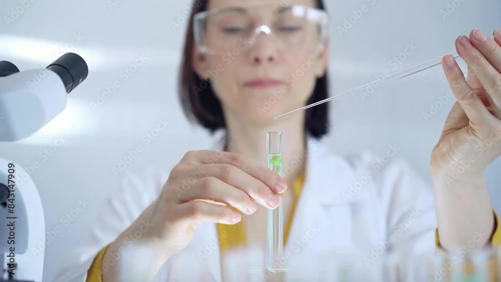 Woman with safety glasses and blue mask is working with lab tubes using a pipette in a modern laboratory, close-up of researcher. Science and medicine