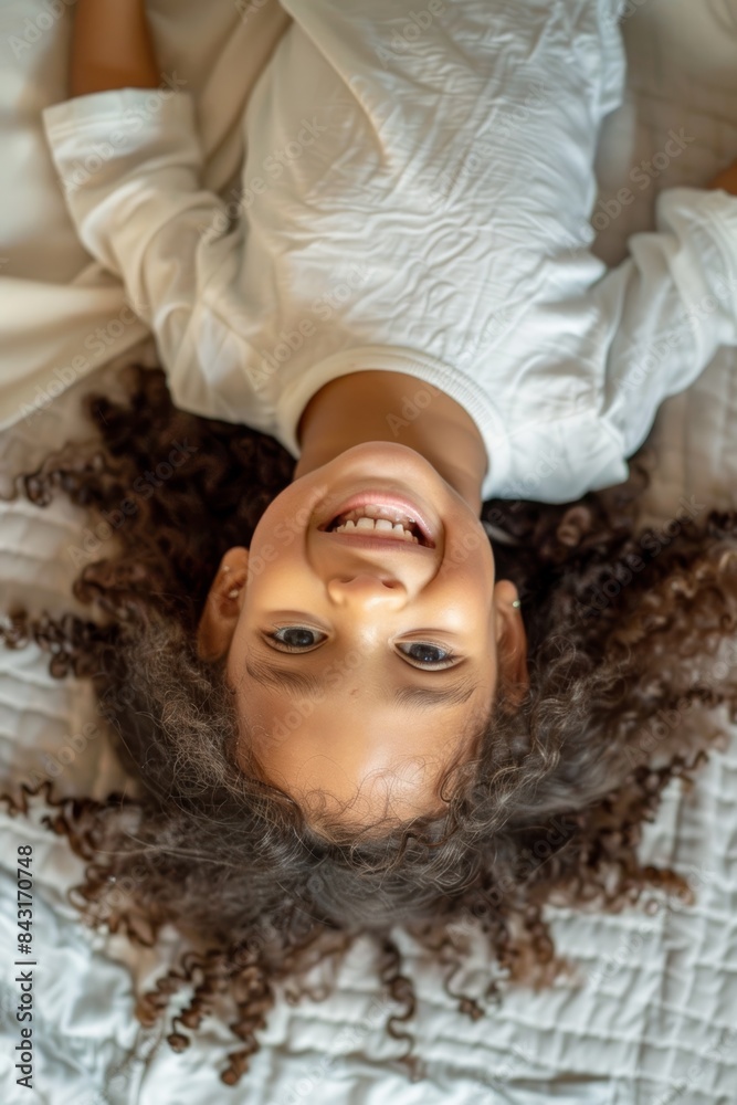 Portrait of youngster laughing and upside down on bed in bedroom, smiling. Happy, smiling youngster or girl laughs at hilarious jokes, comedy, or humor while resting alone.