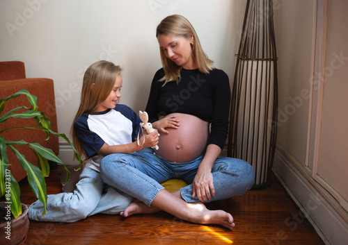 A pregnant mother and her daughter share a joyful moment at home, full of love photo