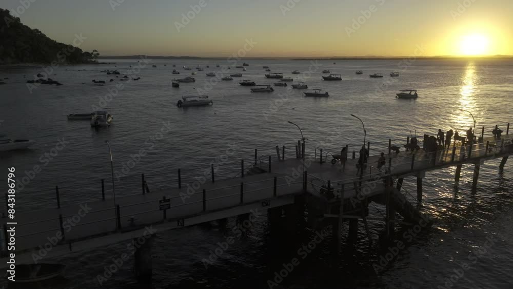 Drone flies along pier with silhouettes fishing as drone heads toward sunset