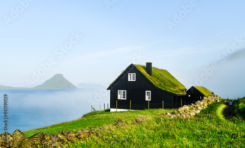 Black wooden faroese house with turf-top grass roof in the Velbastadur village on Streymoy island, Faroe islands, Denmark. Landscape photography photo