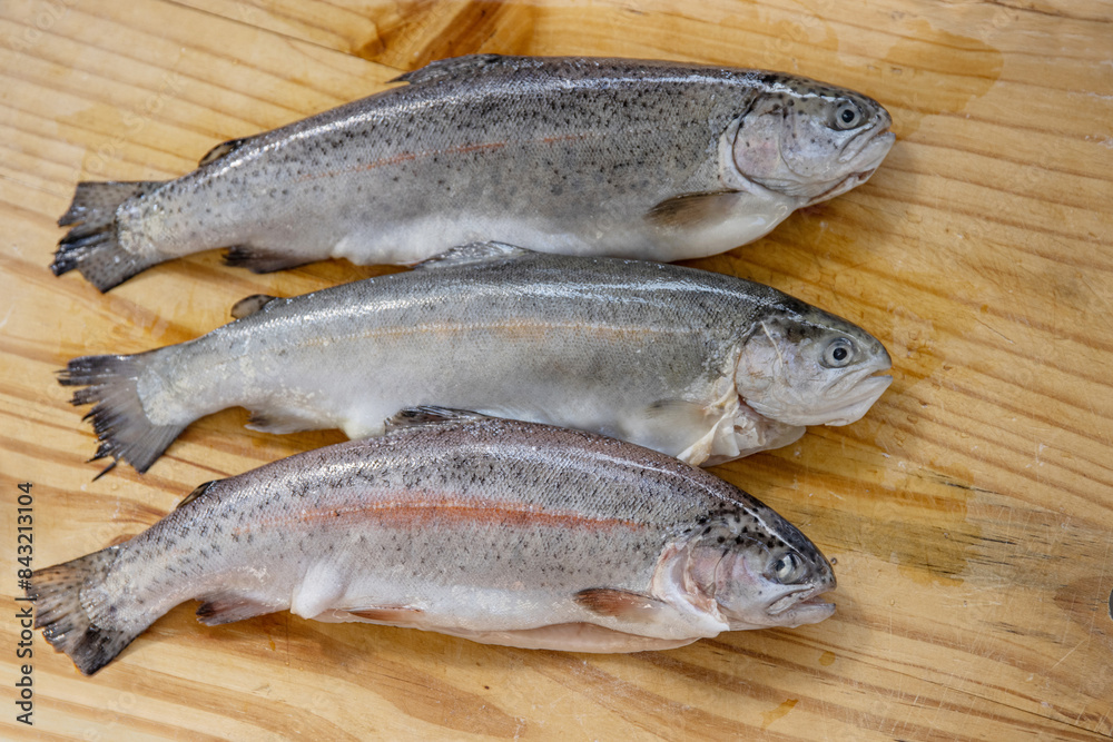 Carving three raw fresh trouts on the old wooden cutting board. Cooking whole freshwater rainbow forel. Oncorhynchus mykiss on the chopping plate. Wood background. Close up. Copy space. Top view Carving three raw fresh trouts on the old wooden cutting board. Cooking whole freshwater rainbow forel. Oncorhynchus mykiss on the chopping plate. Wood background. Close up. Copy space. Top view