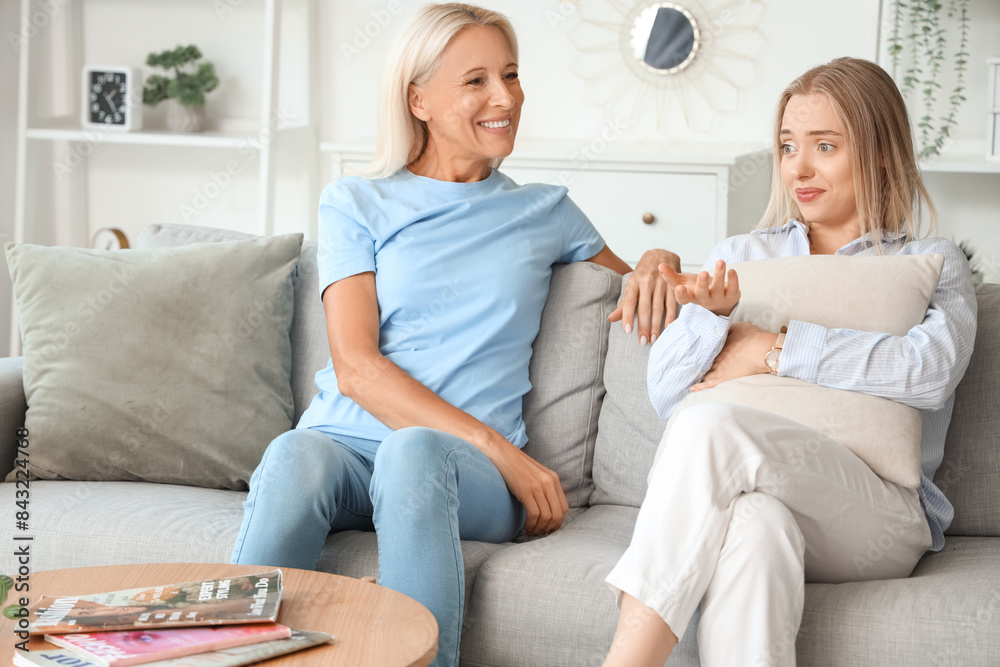 Happy young beautiful woman with her mother sitting in living room and spending time together Happy young beautiful woman with her mother sitting in living room and spending time together