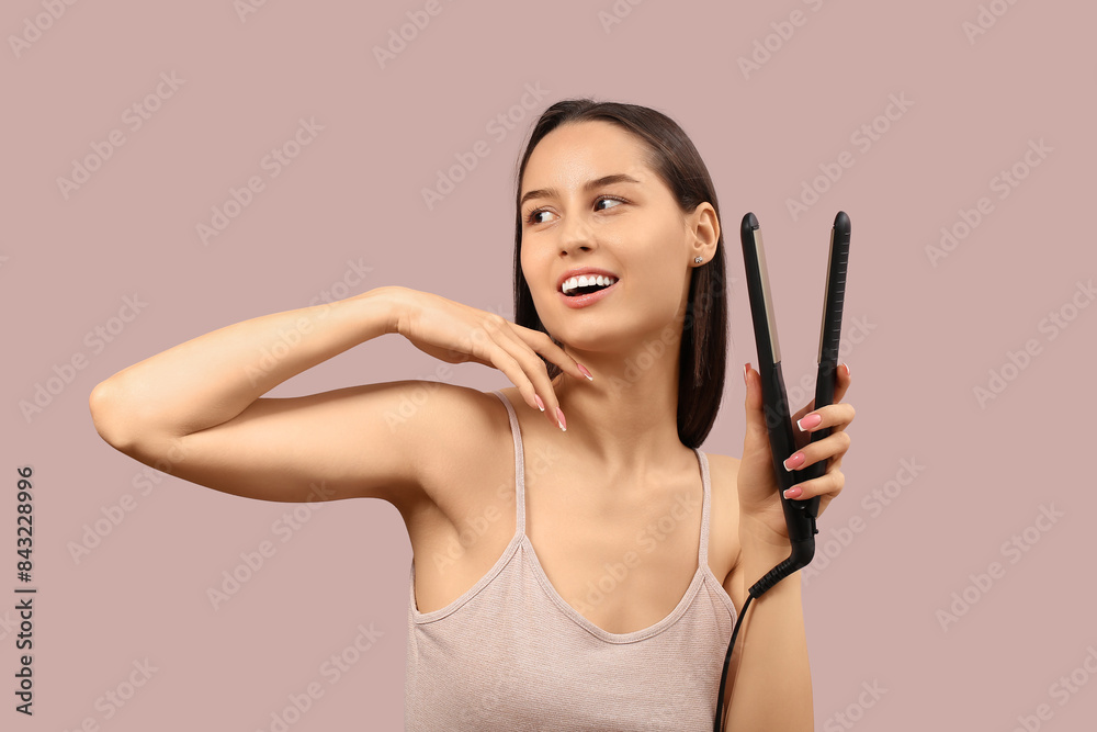 Fototapeta premium Beautiful young woman with hair straightener on pink background