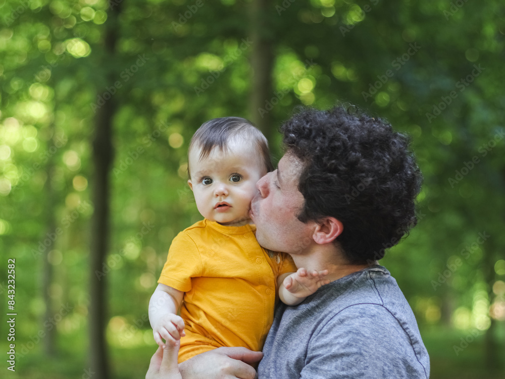 Caucasian young dad holds his little daughter in yellow overalls and gently kisses her on the cheek Caucasian young dad holds his little daughter in yellow overalls and gently kisses her on the cheek