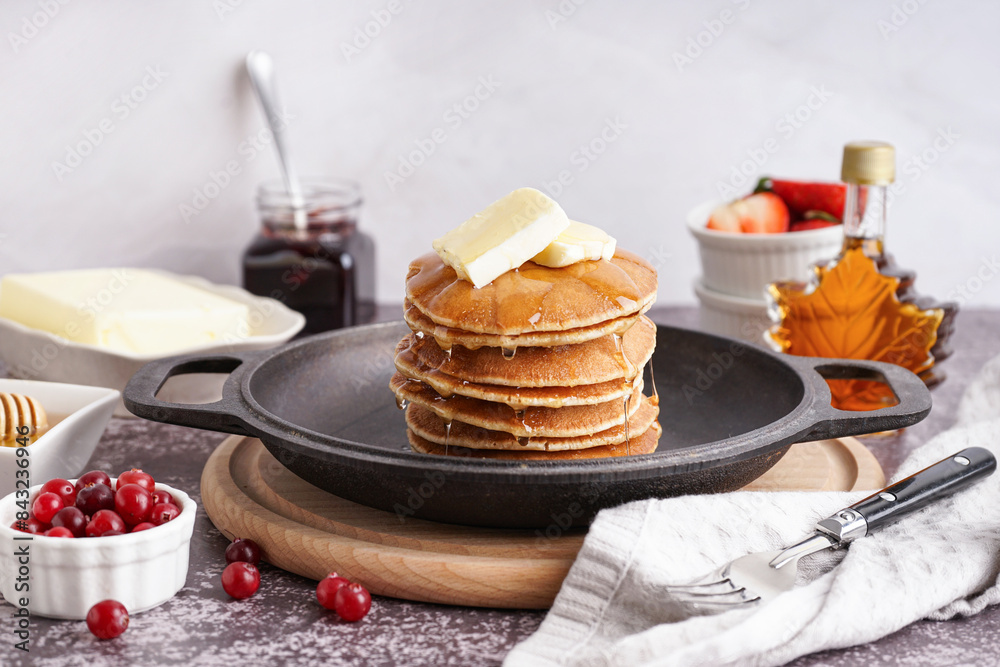 Frying pan with tasty pancakes, butter and fork on grey grunge table against white background Frying pan with tasty pancakes, butter and fork on grey grunge table against white background