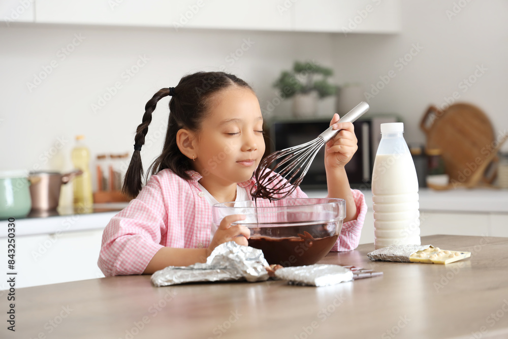 Cute little Asian girl eating melted chocolate in kitchen Cute little Asian girl eating melted chocolate in kitchen