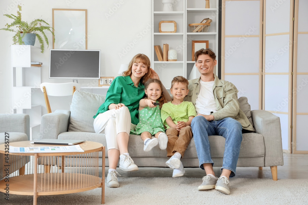 Happy parents with their little children watching TV on sofa at home Happy parents with their little children watching TV on sofa at home
