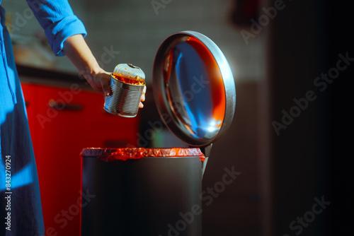 Woman Throwing Away a Spoiled Can of Food . Hand of a person disposing of uneaten expired can 
 photo