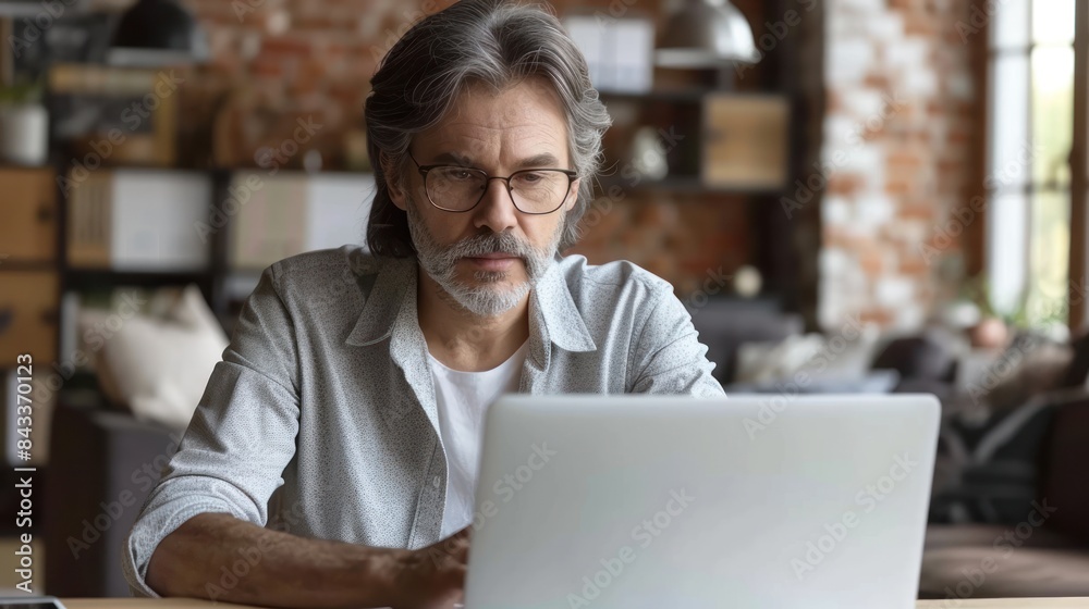 A man sits at a desk in a modern loft, intently focused on his laptop A man sits at a desk in a modern loft, intently focused on his laptop